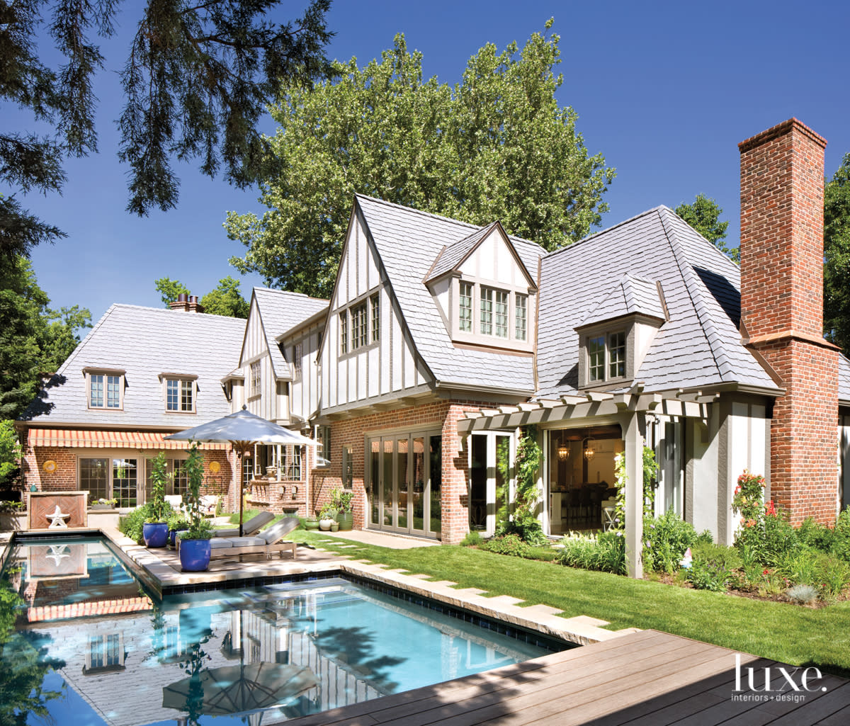 Backyard of a Tudor house. A bright blue pool sits in the green grass.