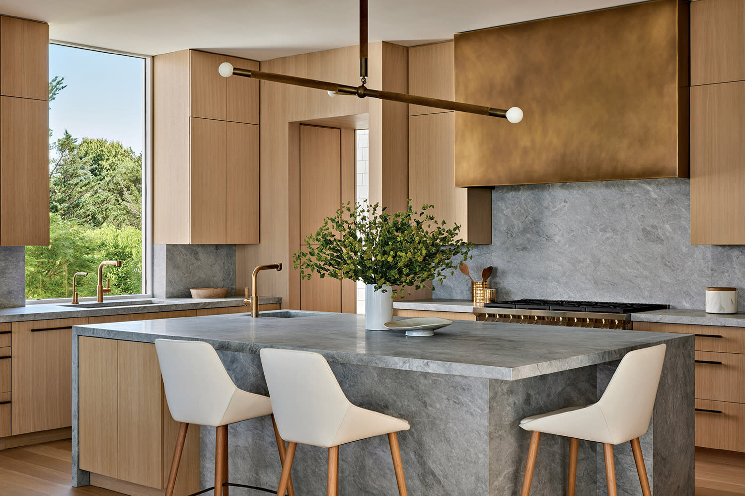 contemporary kitchen with a bronze range hood, gray marble countertops and an Apparatus pendant