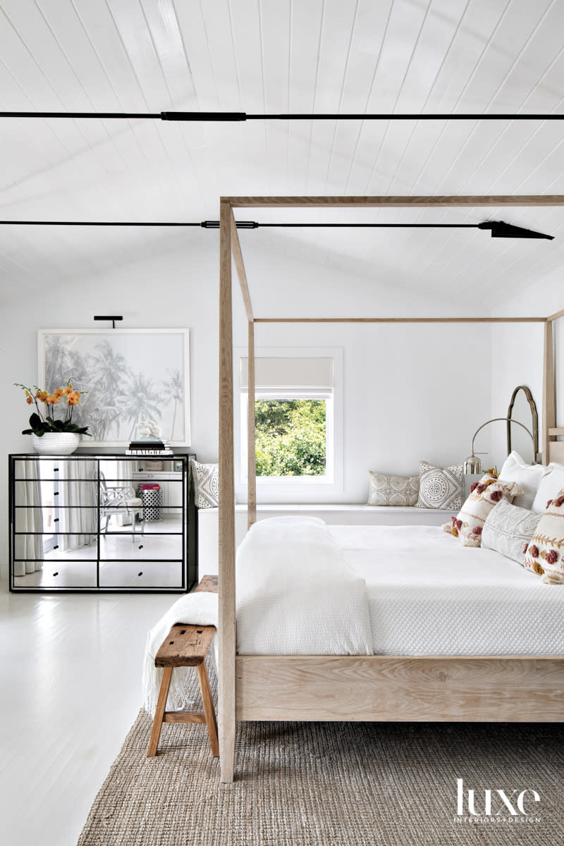 white primary bedroom with wood four-poster bed, mirrored dresser and black ceiling tension rods