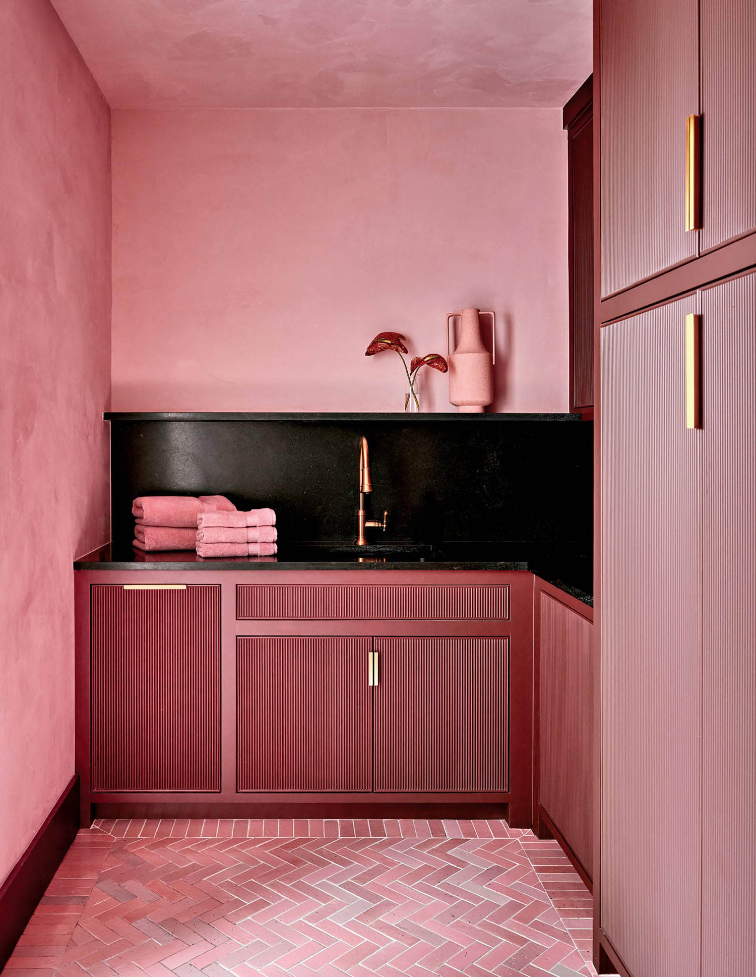 A small, modern pink laundry room with stylish cabinetry, black countertop and gold fixtures