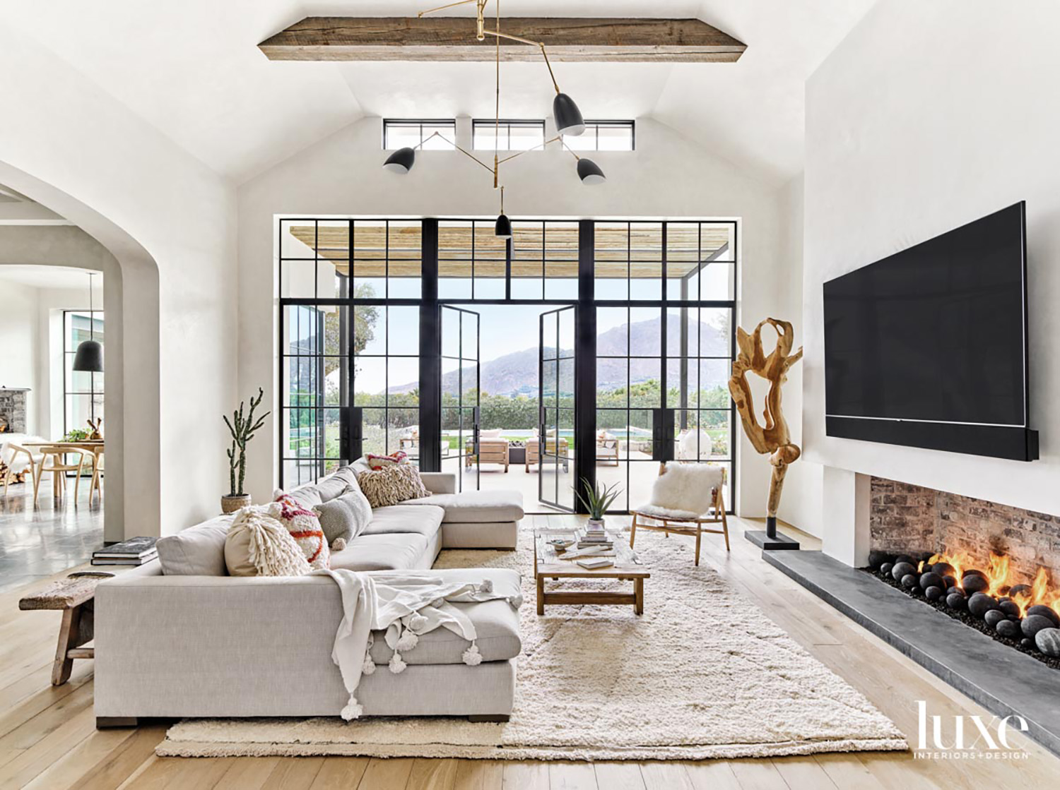 A living area with a large gray sectional in front of a fireplace with a TV over it.