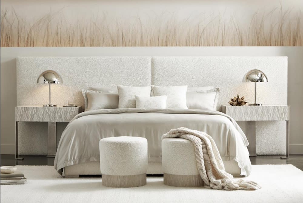 An all white bedroom with large white padded headboard, decorative side tables and chrome lamps.