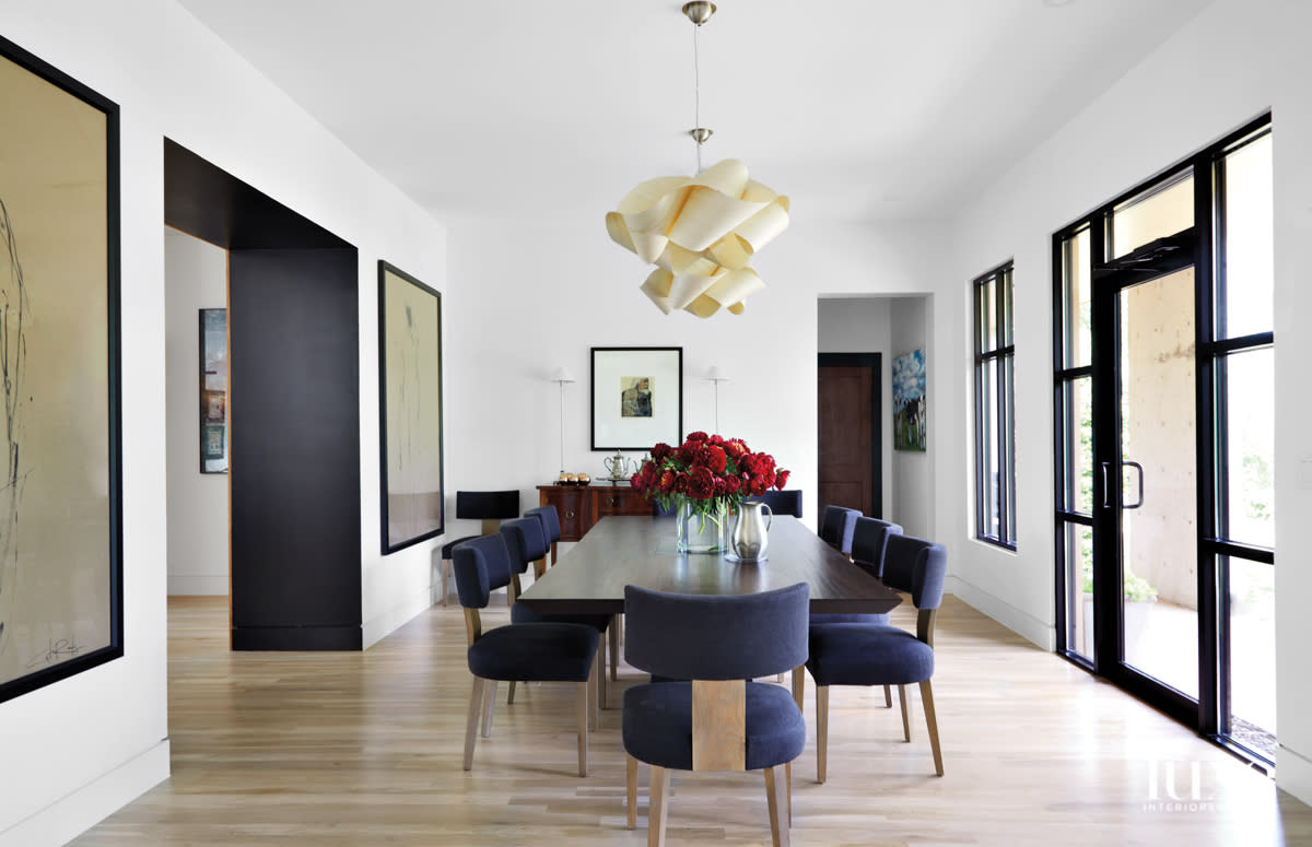 Minimalist dining room with klismos dining chairs, extra-wide door frame painted black, and a sculptural ceiling fixture