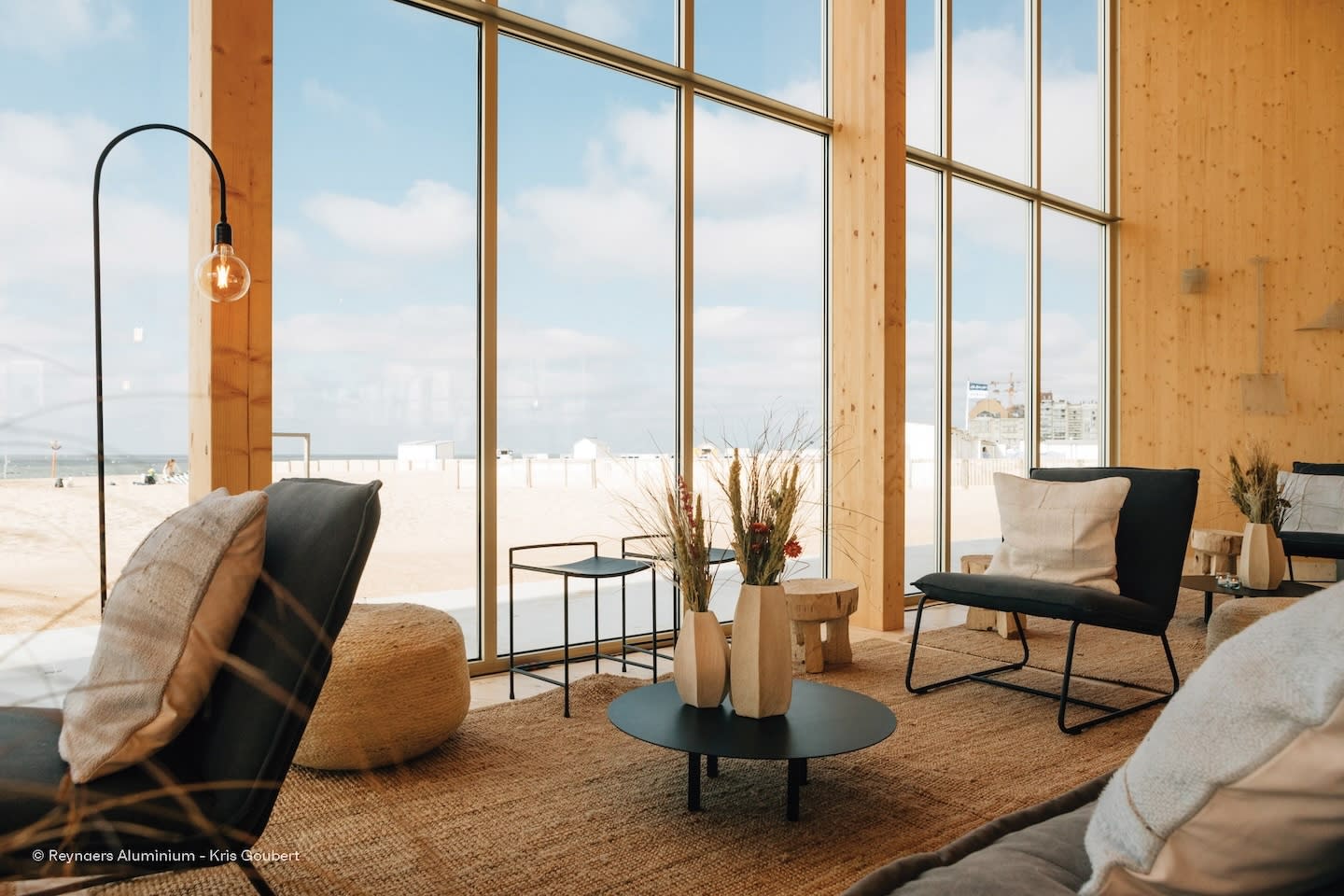 Modern beachside lounge with large windows. Cozy seating, neutral tones, decorative vases, and warm lighting create a serene, inviting atmosphere.