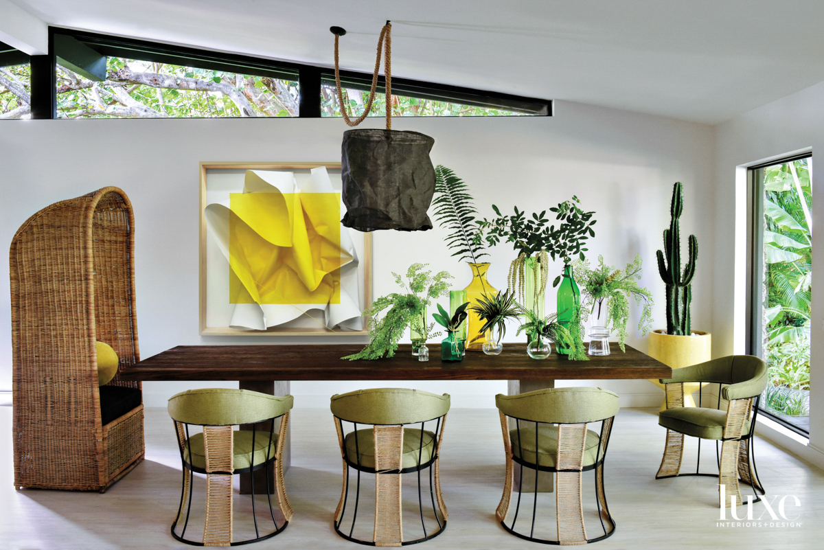 dining area with rectangular wood table, large rattan head chair, yellow artwork, black pendant and plants