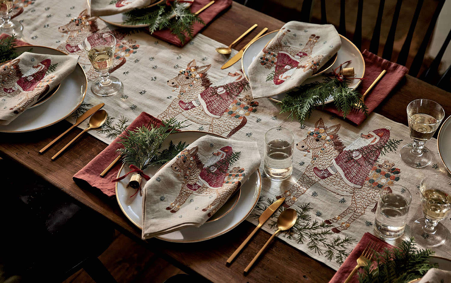 A dining table with a red tablecloth, matching cloth napkins and festive holiday place settings.