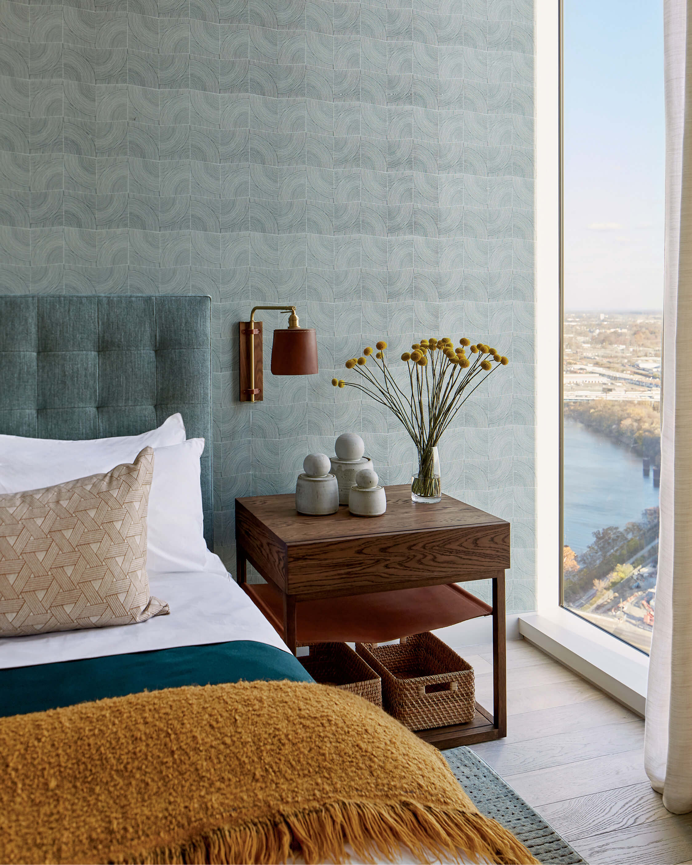 teal wallpaper above a teal upholstered bed with mustard yellow linens