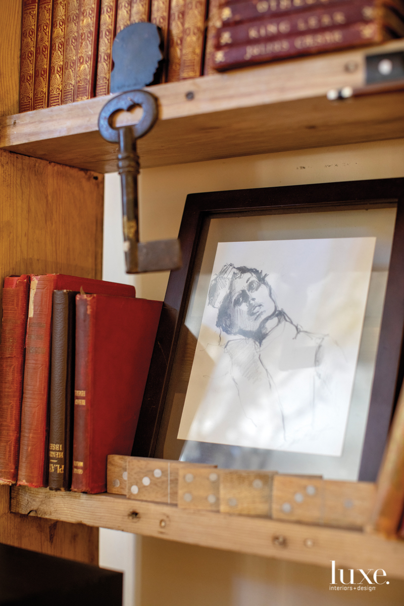 A pencil drawing rests on a shelf amid books and dominoes.