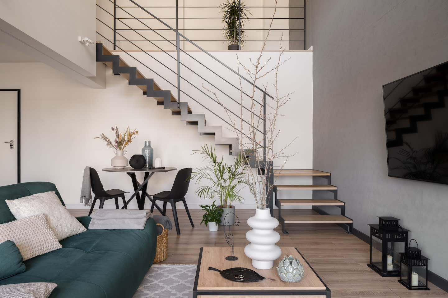 Modern living space with green sofa, floating stairs, and dining area by Bayside Home Improvement.