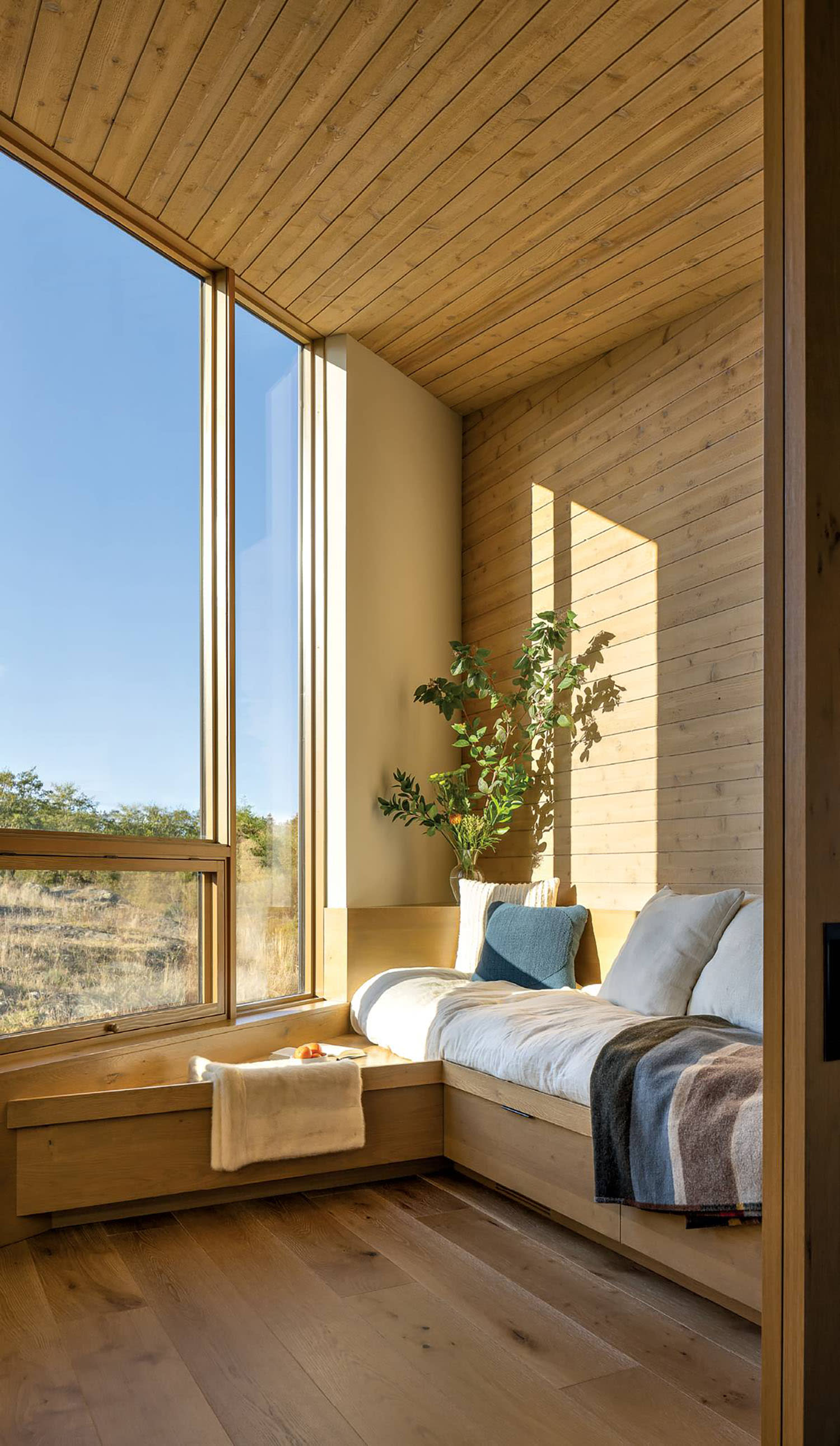 A small sitting area near a window, made up with pillows and a colorful throw blanket.
