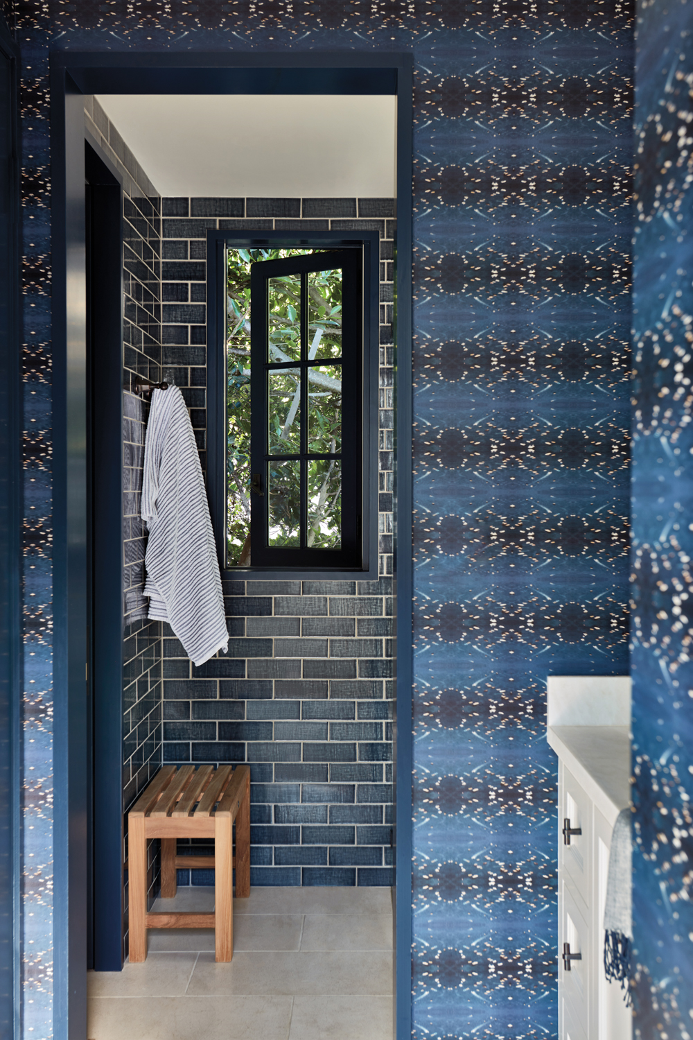 blue wallpapered bathroom with a blue tile shower