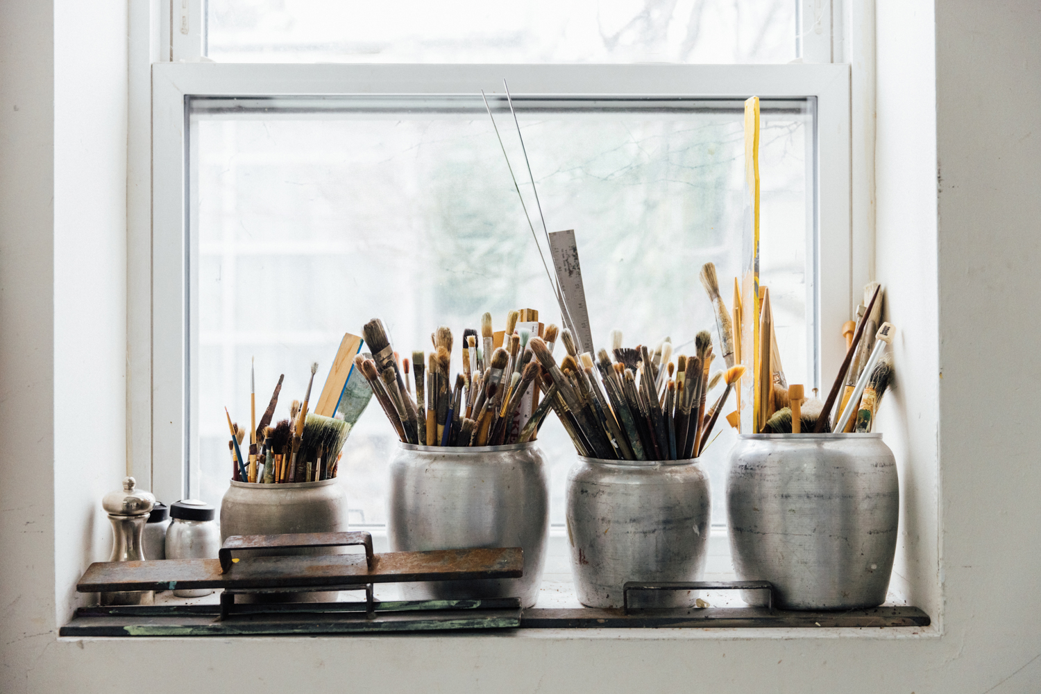 metal containers containing paint brushes sit on a window sill