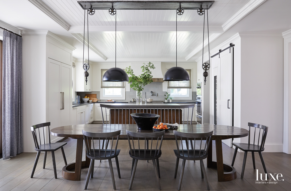 A kitchen seating area has a long table and a dramatic, pulley-operated light fixture.