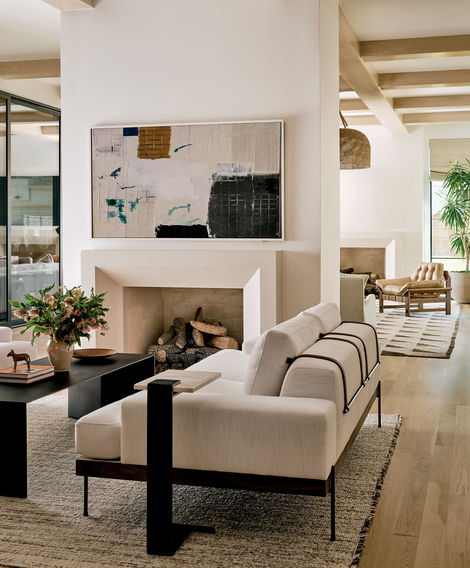A modern living room with a minimalist design, featuring a white sofa, abstract art above a fireplace, a black coffee table with a plant, and a light wood floor.