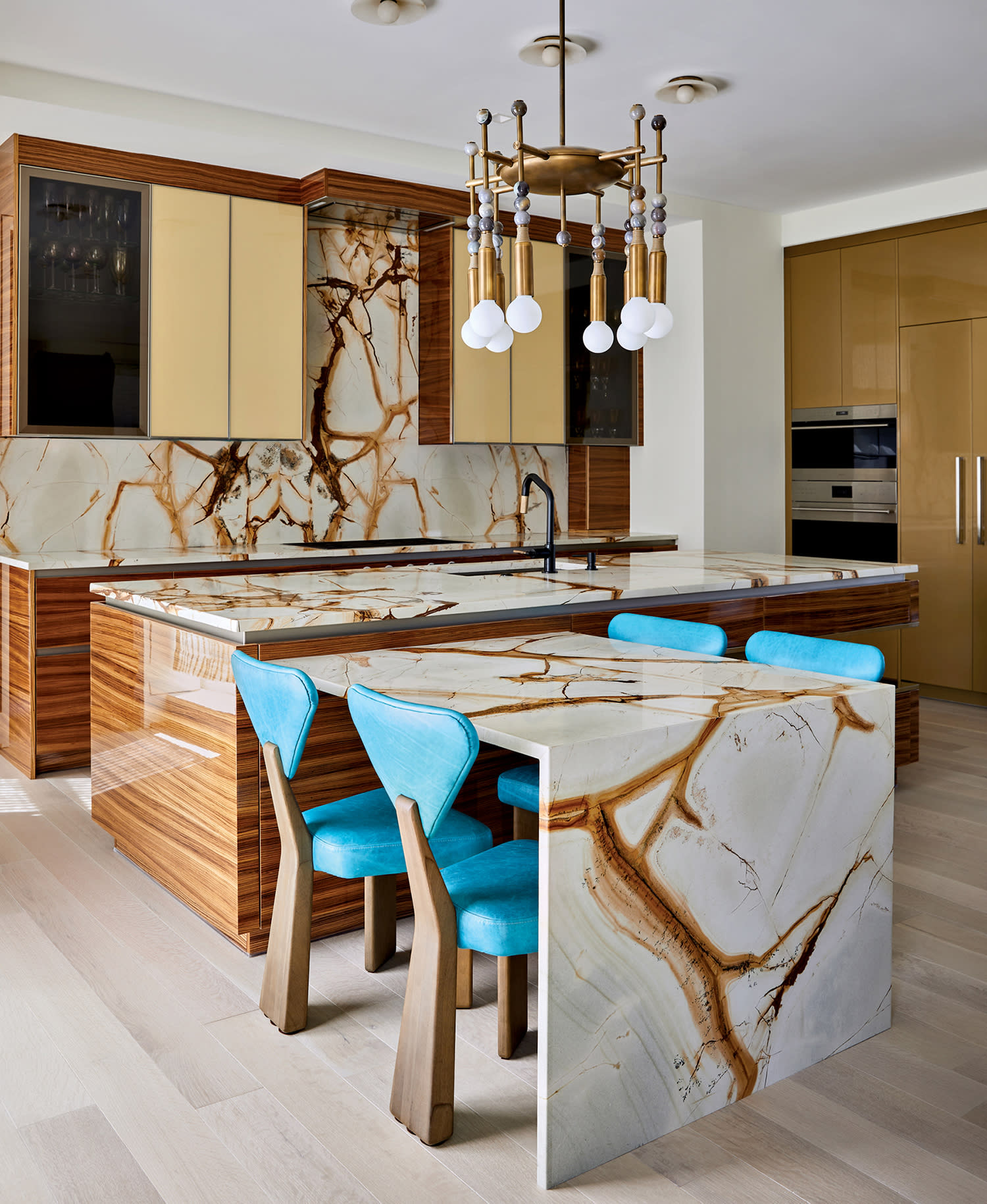 modern kitchen with tigerwood cabinetry and blue sculptural barstools around a marble island