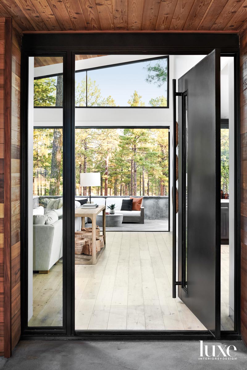 A door opens to a living room with windows that look out on trees.