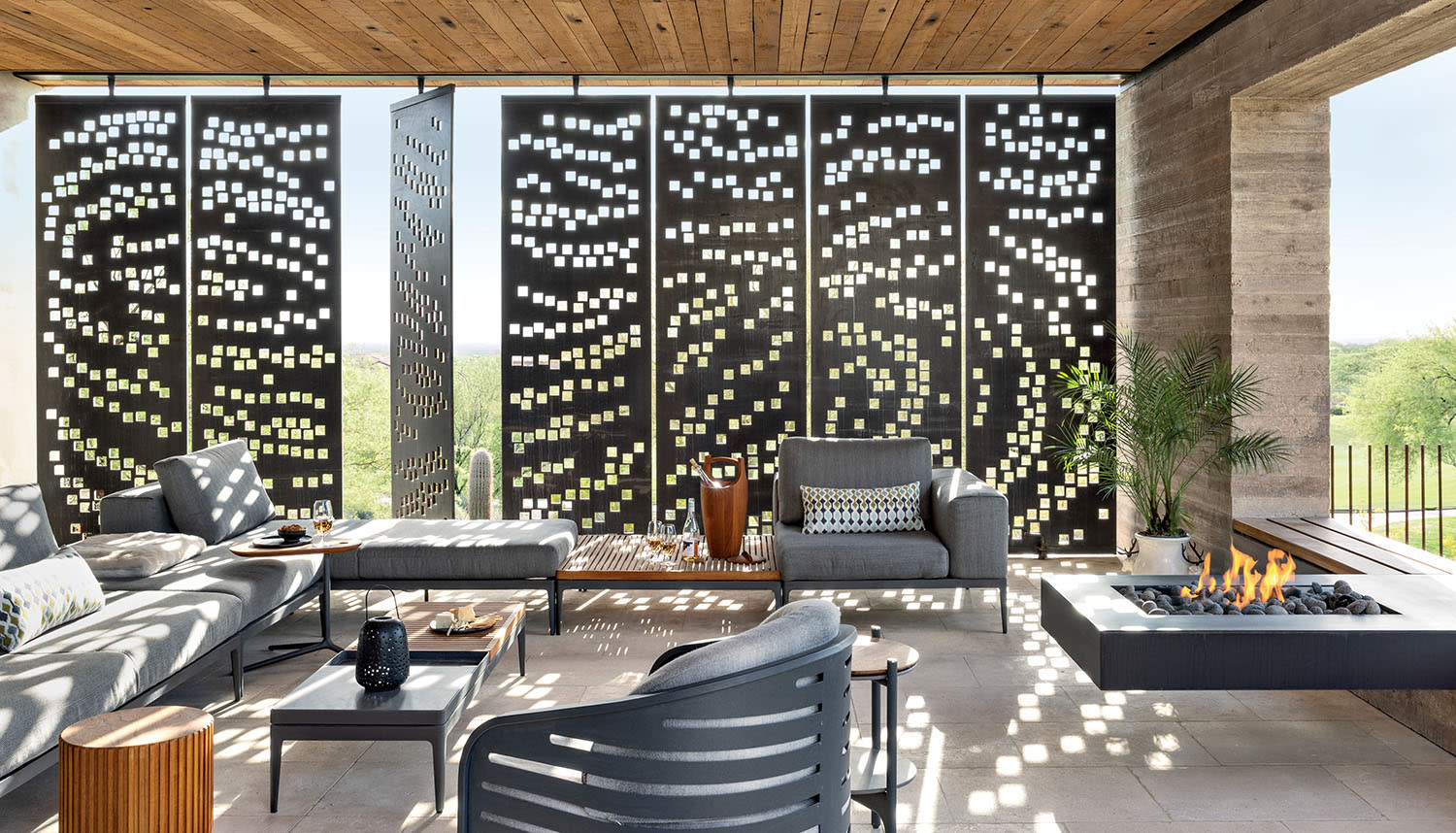 Perforated steel panels let light into an outdoor seating area with couches, tables and a fireplace.