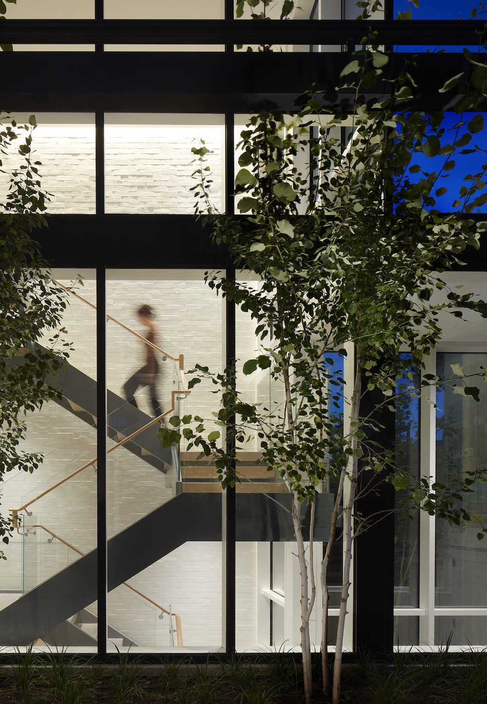 Exterior view that has floor to ceiling windows showcasing the steel and wood staircase.