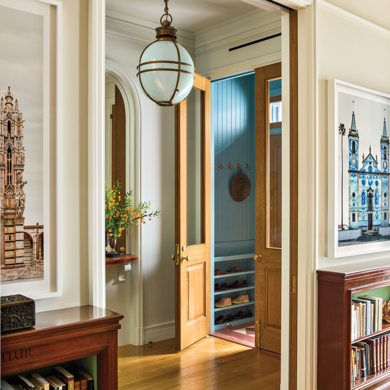 Stylish hallway with wooden flooring, a globe light fixture, and framed architectural art. A door opens to a blue closet with shoe shelves. Cozy and elegant.