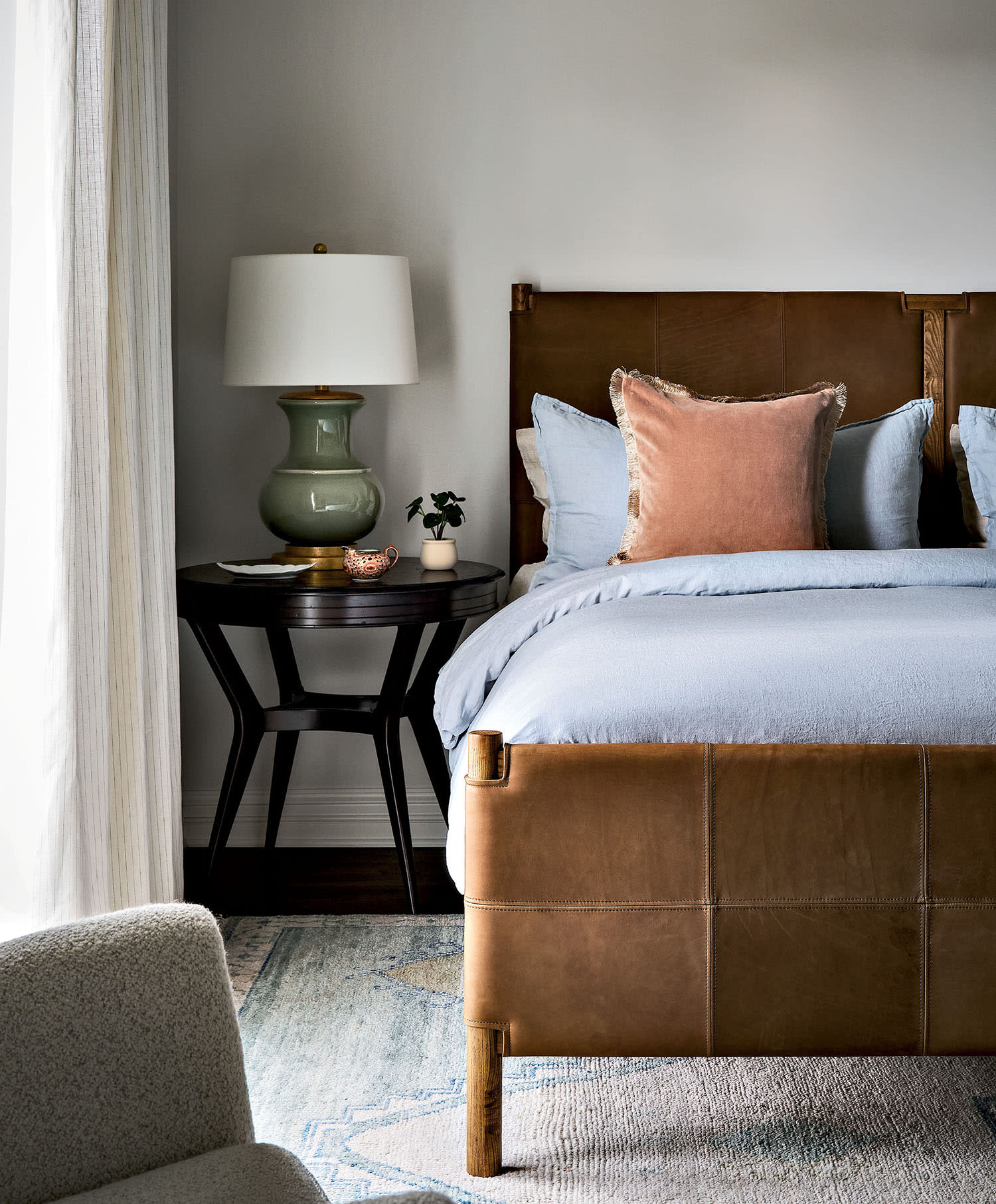 A side table rests next to a bed with blue and pink linens, sitting on top of a light-colored rug.