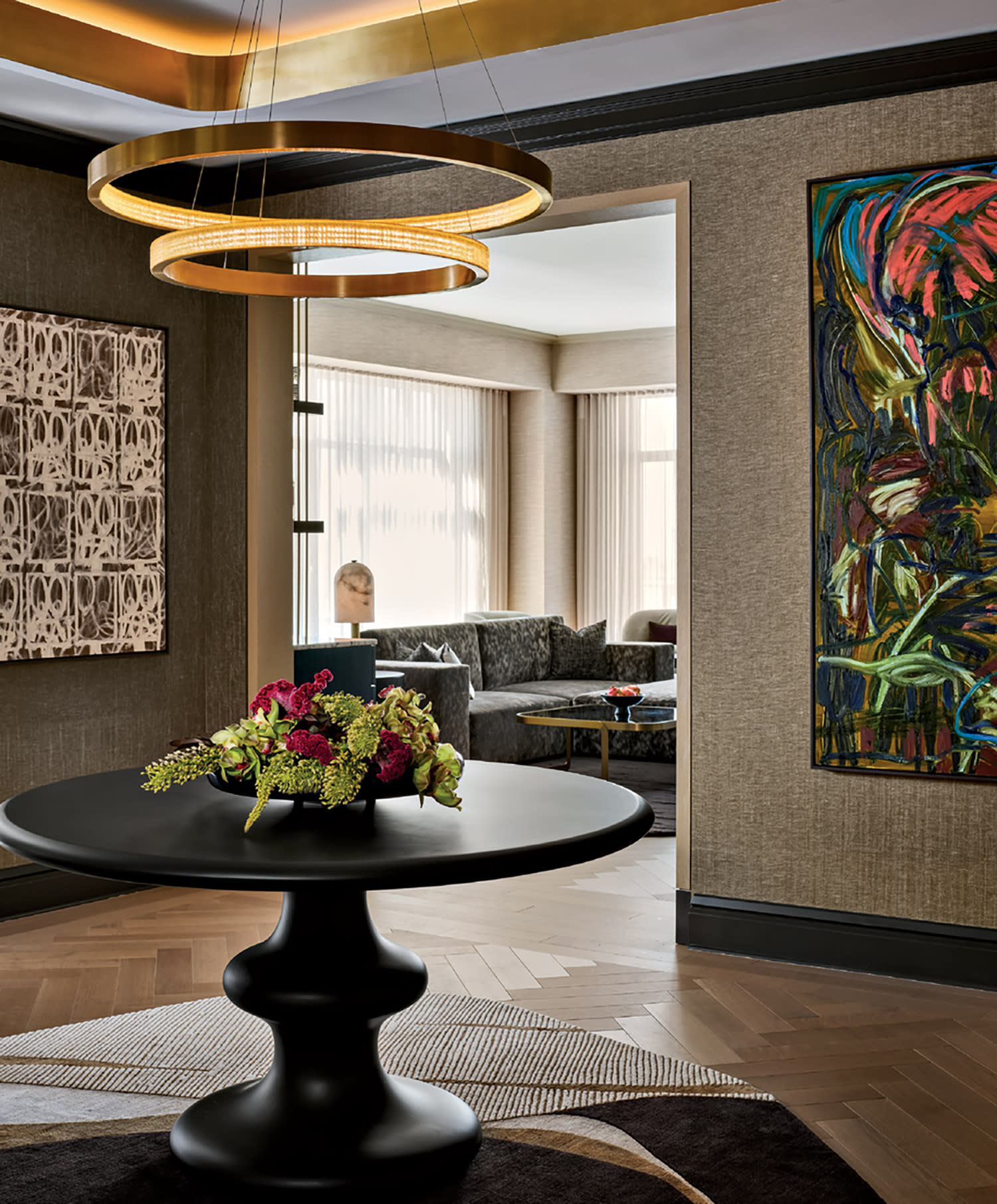 A modern room with a black round table and colorful flowers. Circular ceiling lights, abstract paintings, and a cozy seating area create a stylish ambiance.