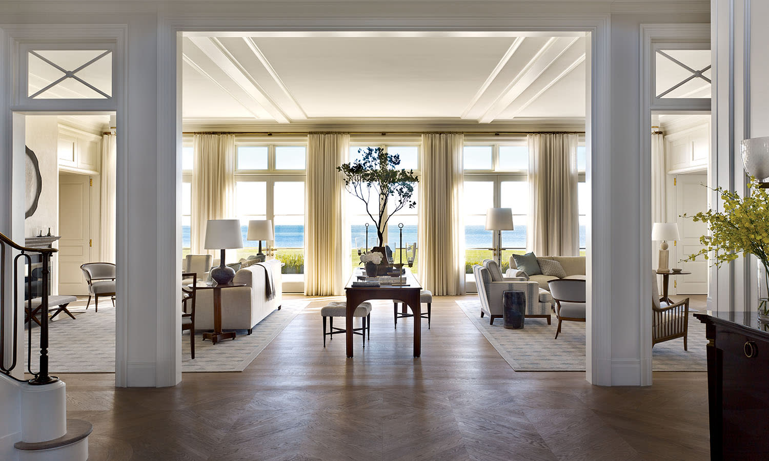 Spacious living room with cream walls, large windows, and ocean views. Elegant wood floors and soft lighting create a calm, luxurious ambiance.