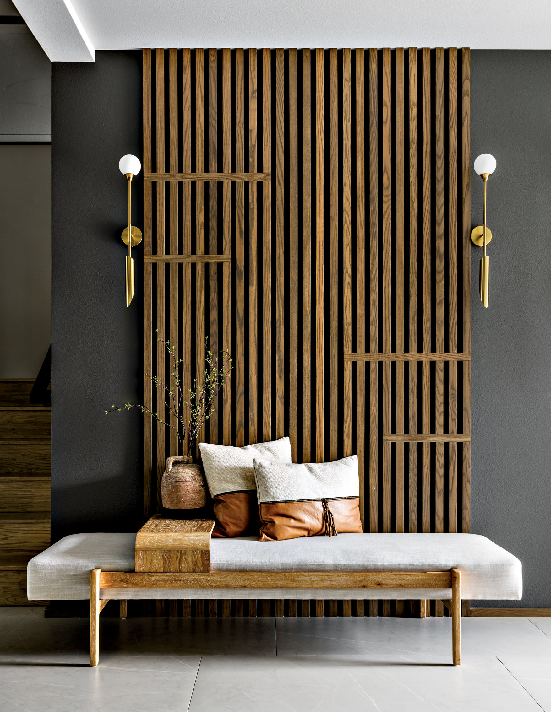 entryway with a slatted wood wall behind a bench and midcentury-inspired sconces