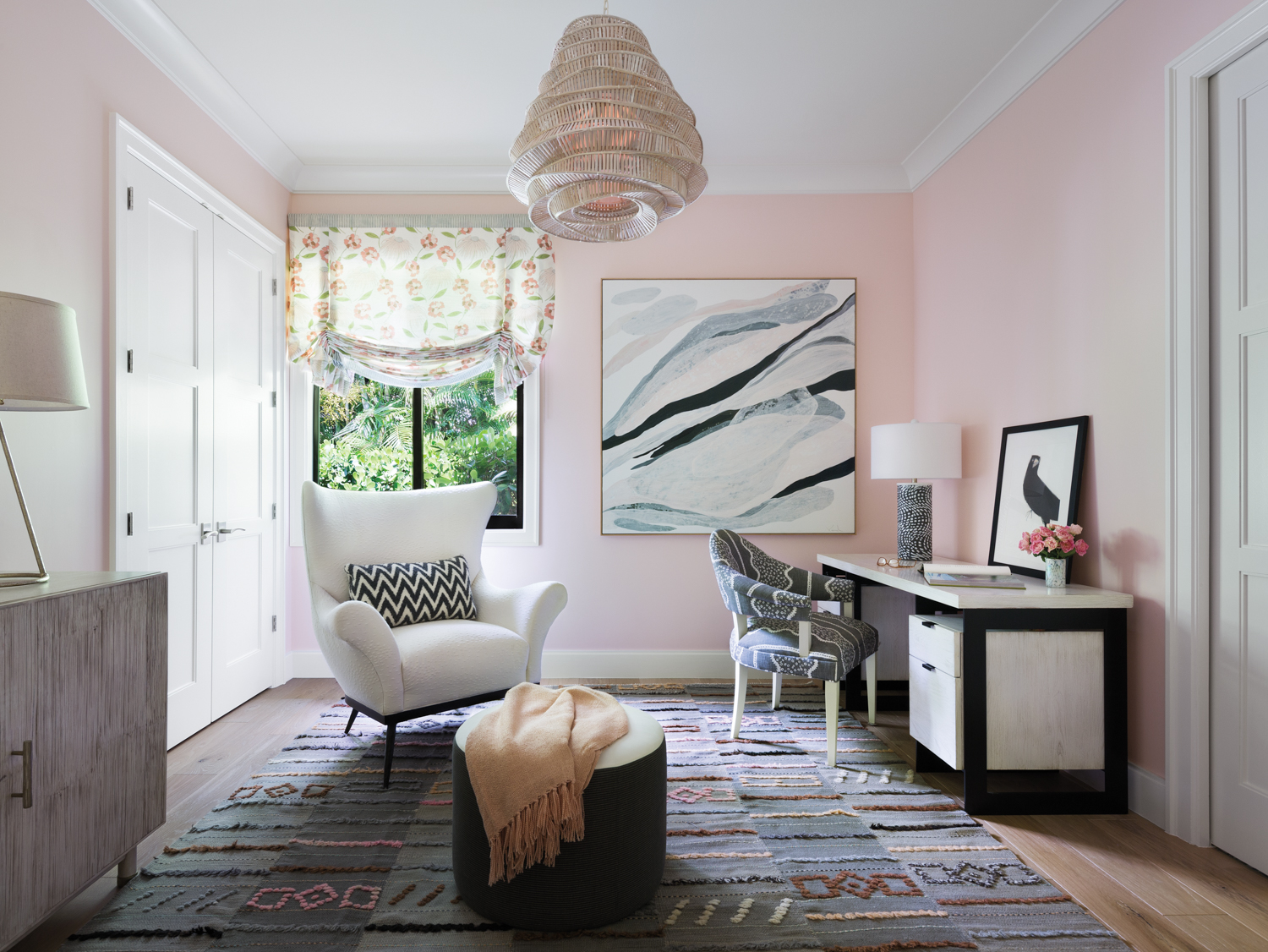 Pink office with pink walls, patterned rug and white armchair