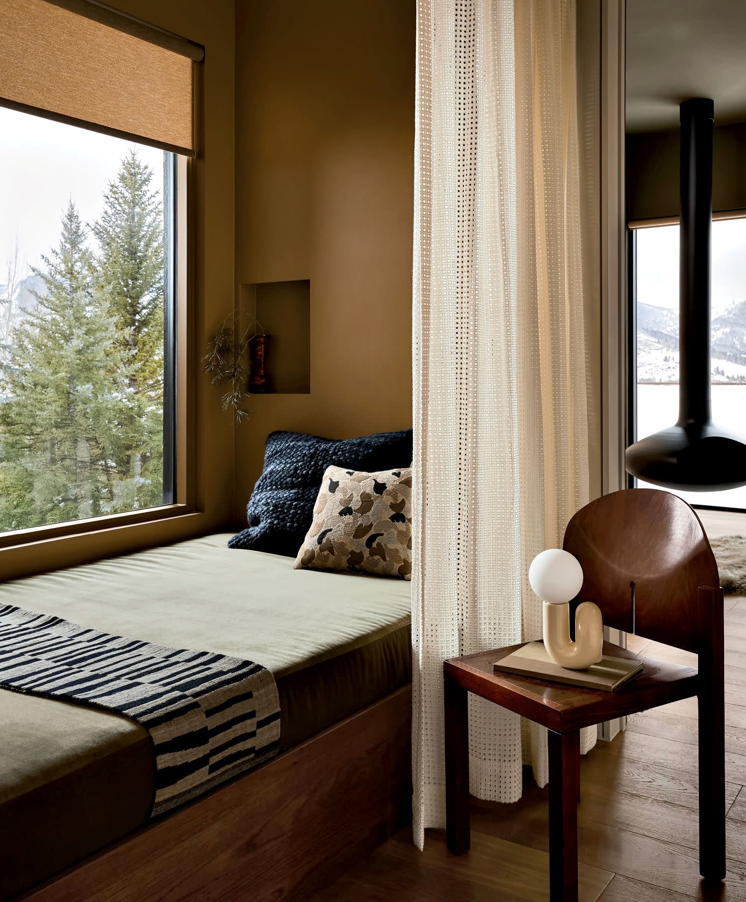Cozy room featuring an earth-toned daybed with patterned cushions and a large window view of snowy trees