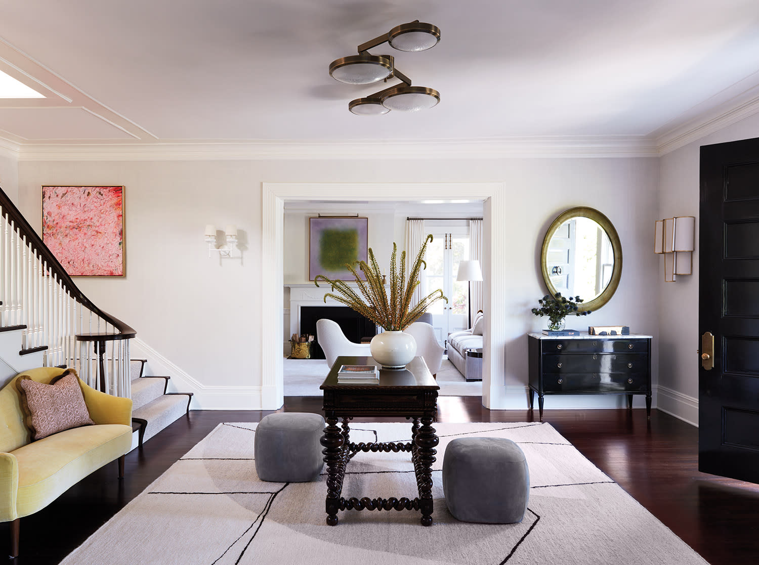 Sophisticated living room with a modern chandelier, a round mirror on the right, geometric rug, and abstract art. Warm, inviting, and elegant decor.