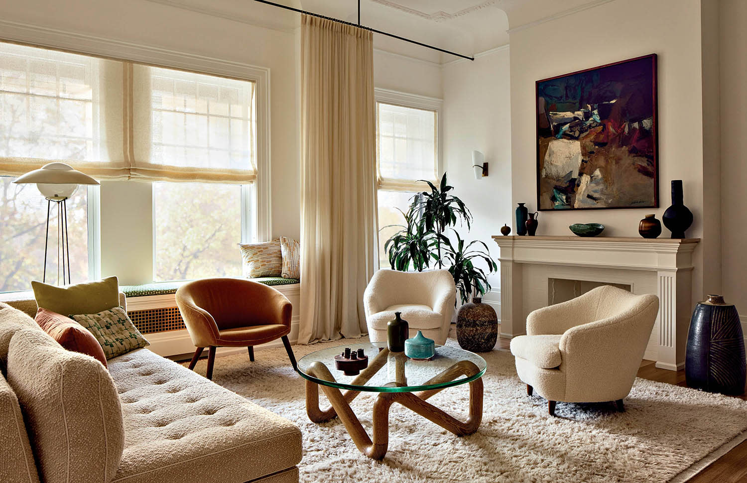 A coffee table with angular legs is encircled by a couch and armchairs with a fireplace behind.