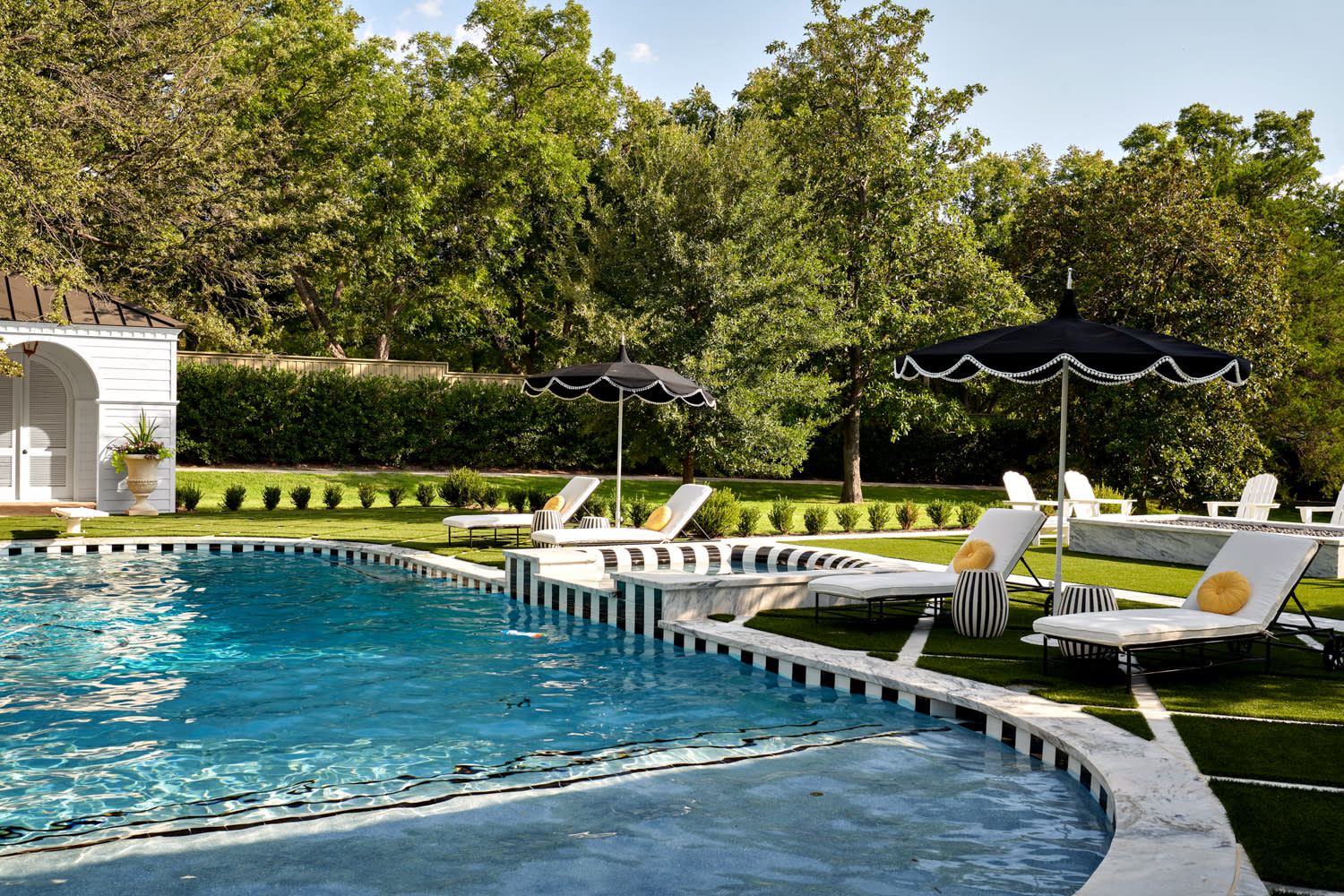 A swimming pool surrounded by a white fence, reflecting a clear blue sky.