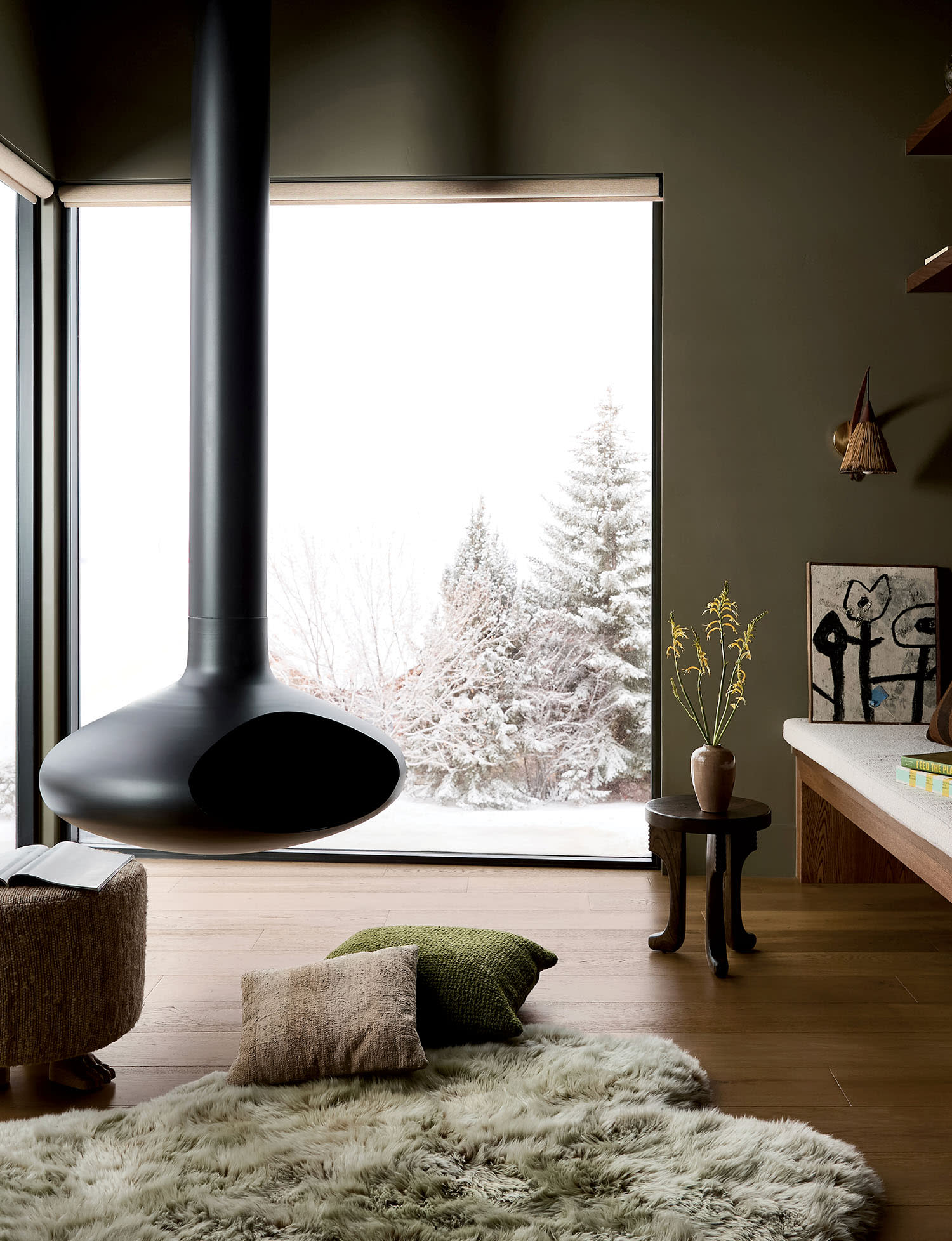 A multipurpose office area with a hanging fireplace set near windows looking out on a snowy backdrop.