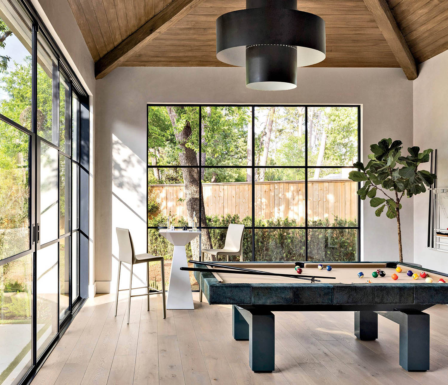A game room with a billiard table and a high table and barstools in a corner near the windows.