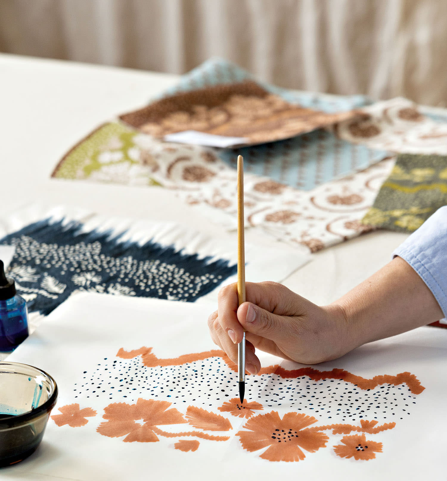 A designer paints a floral design on a canvas with other designs nearby.