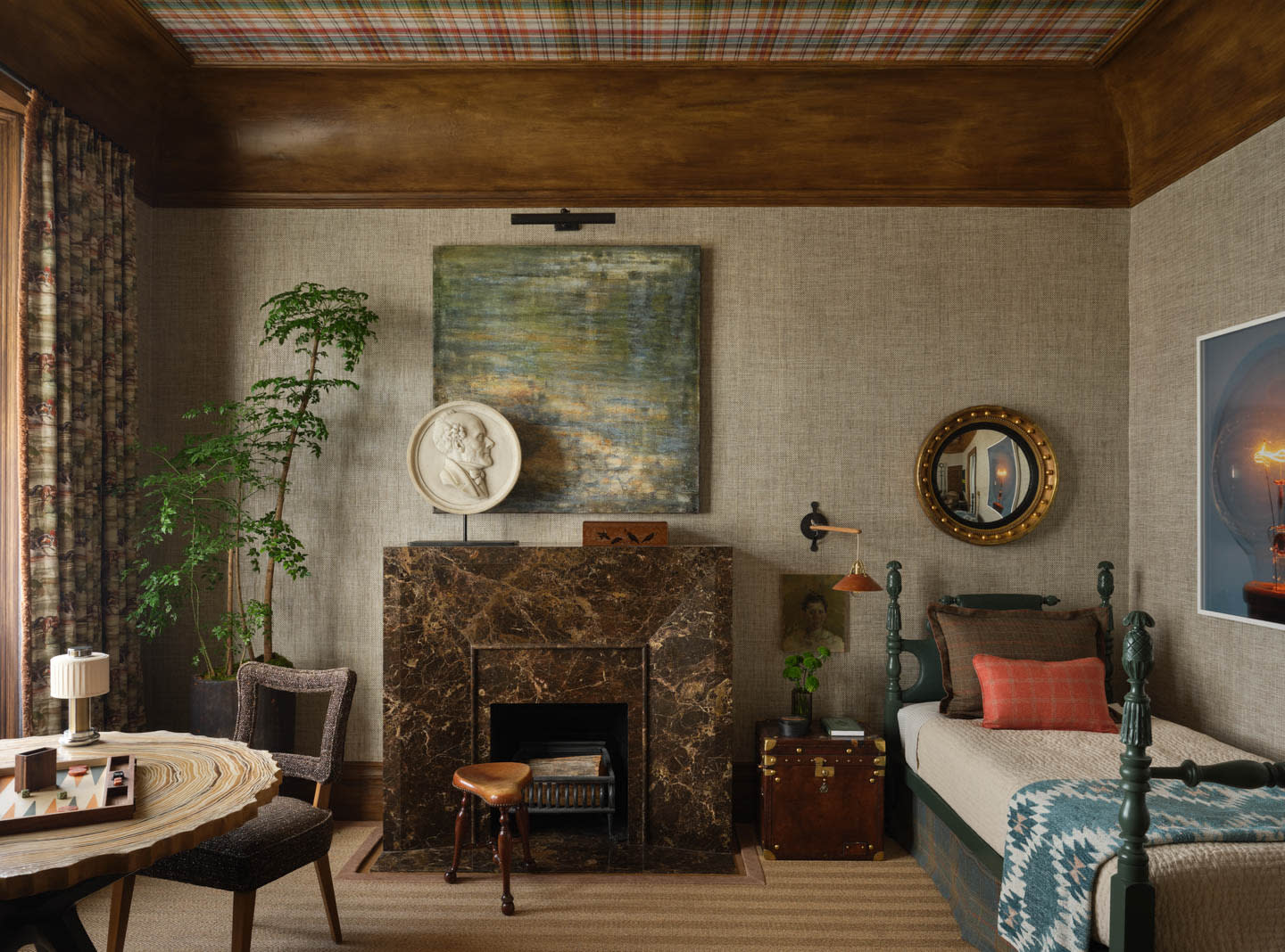 Cozy room with a marble fireplace, plaid ceiling, and textured walls. Features a round table, patterned curtains, and a daybed with colorful pillows.