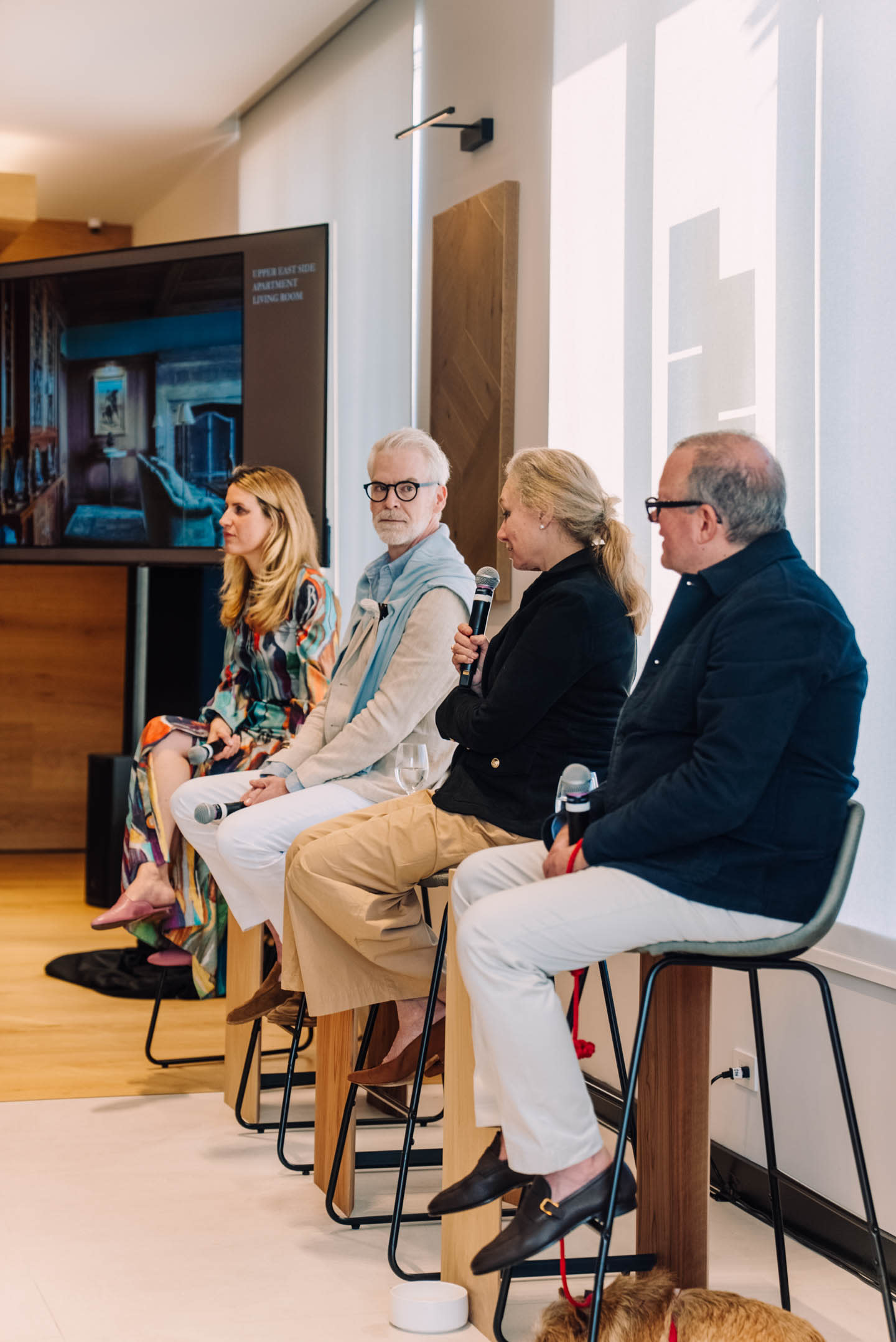 Four individuals sit on high stools in a modern room, engaged in a panel discussion.