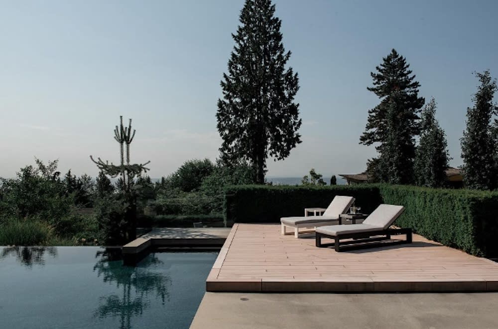 Relaxing outdoor pool area with deck, lounge chairs and greenery for privacy.