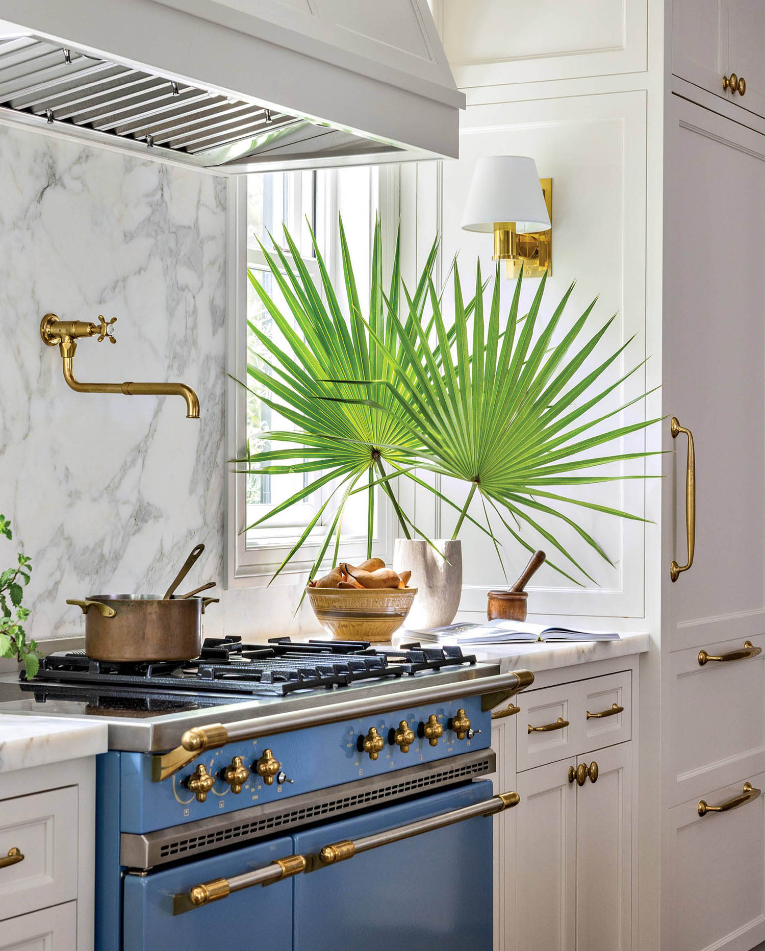 A blue stove sits nestled between white cabinets kitchen cabinets with brass accents and sconces.