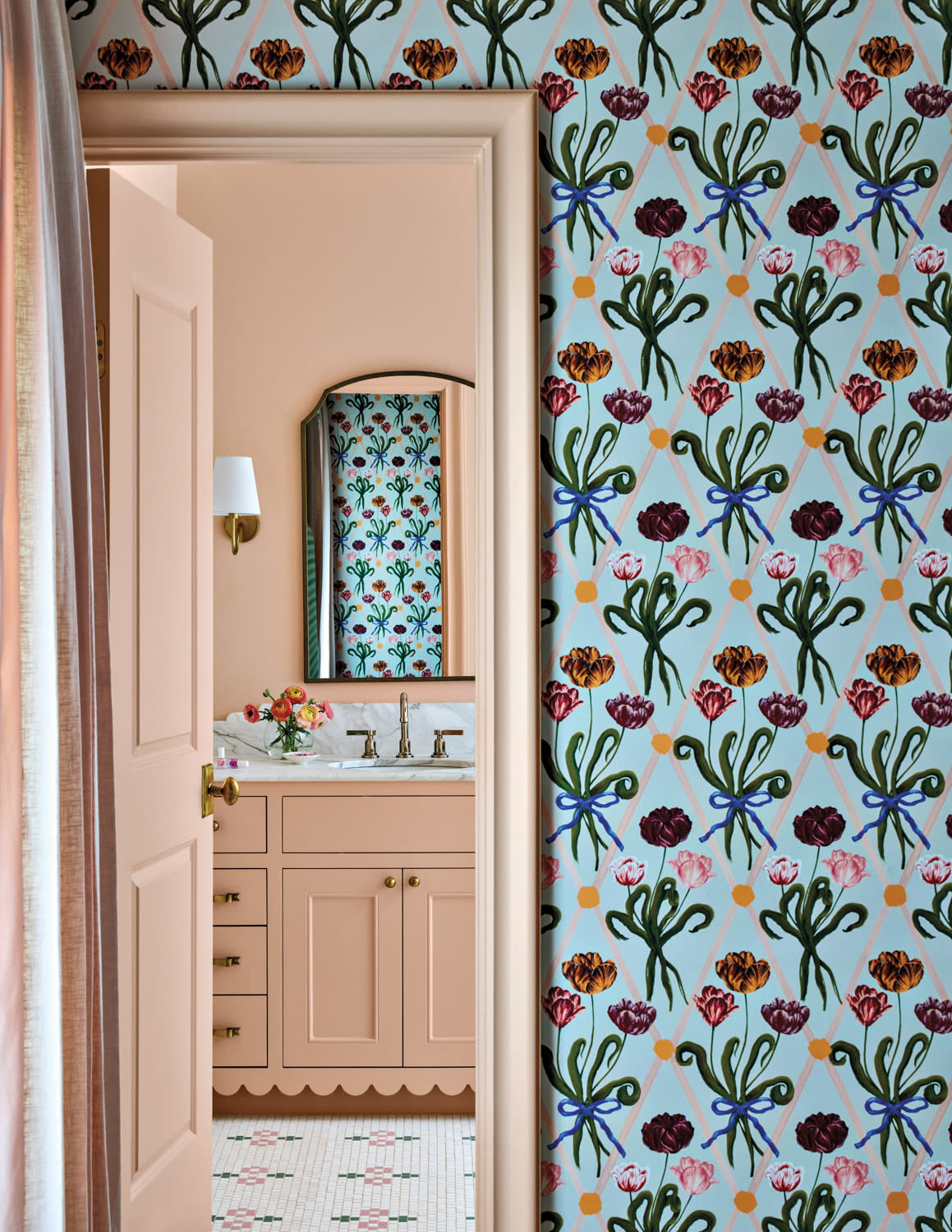 Colorful floral wallpaper with vibrant patterns leads to a peach-toned bathroom. Elegant vanity with flowers and a mirror reflects the lively design, creating a cheerful ambiance.