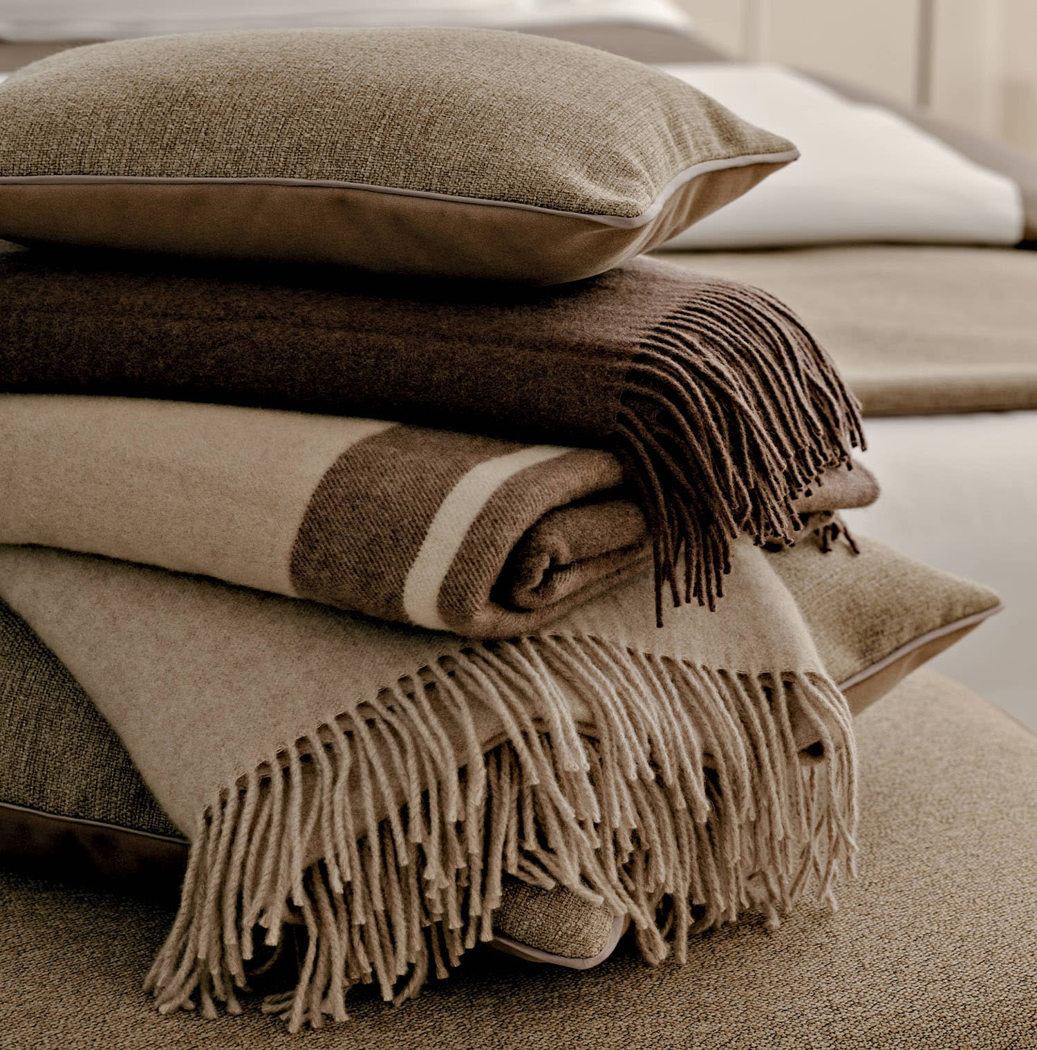 Throw blankets and pillows in neutral tones piled on top of one another.