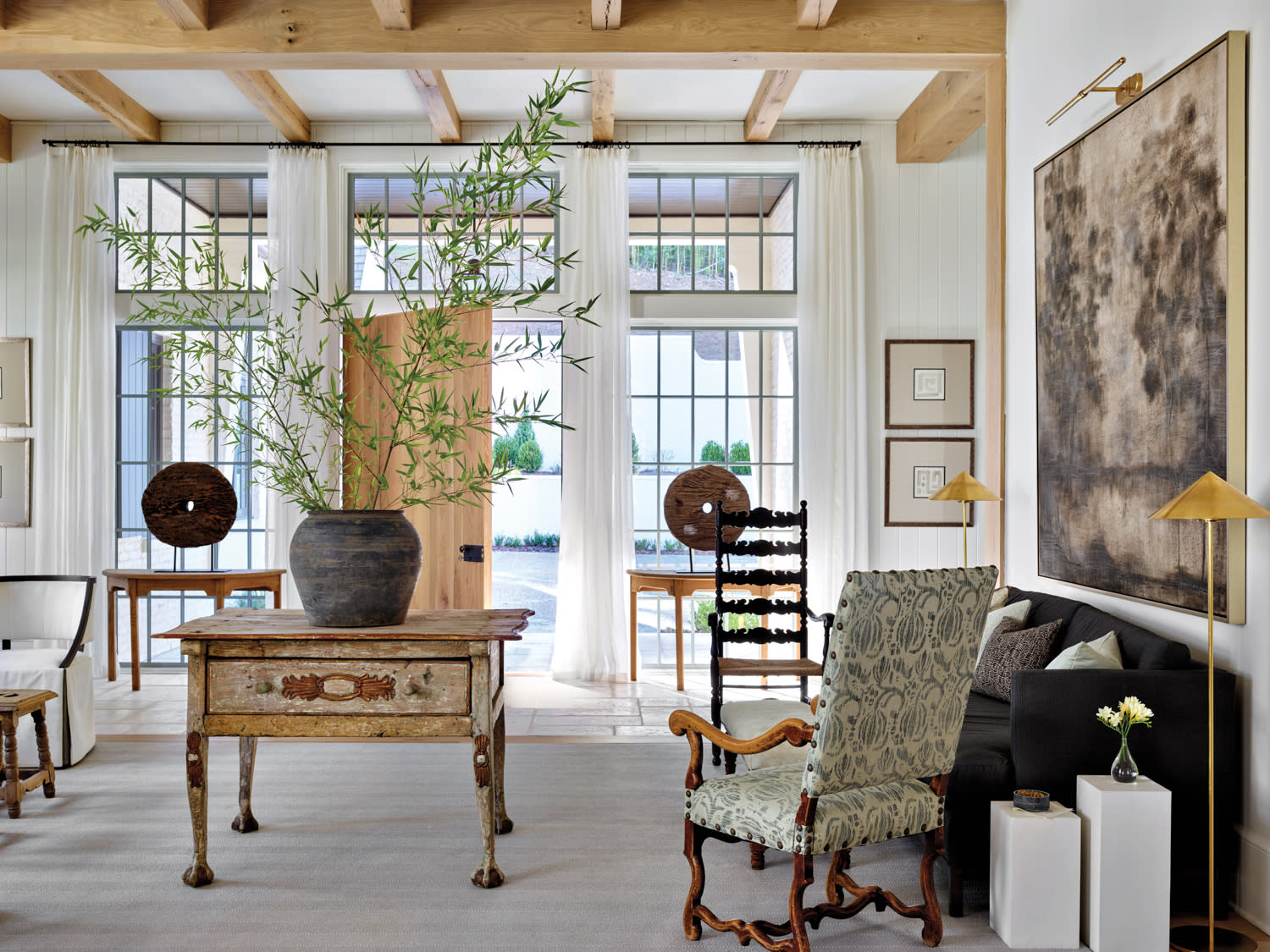 Light-filled salon with center table, consoles flanking front door, antique worktable and white sofa