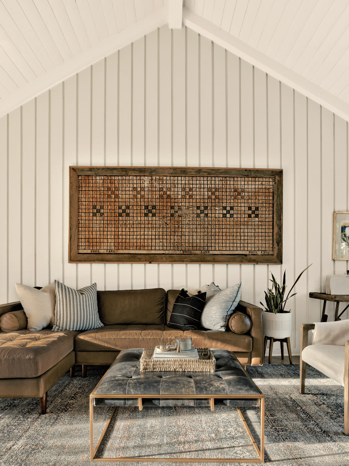 Antique game board hanging above a brown leather couch in a white living room with shiplap walls