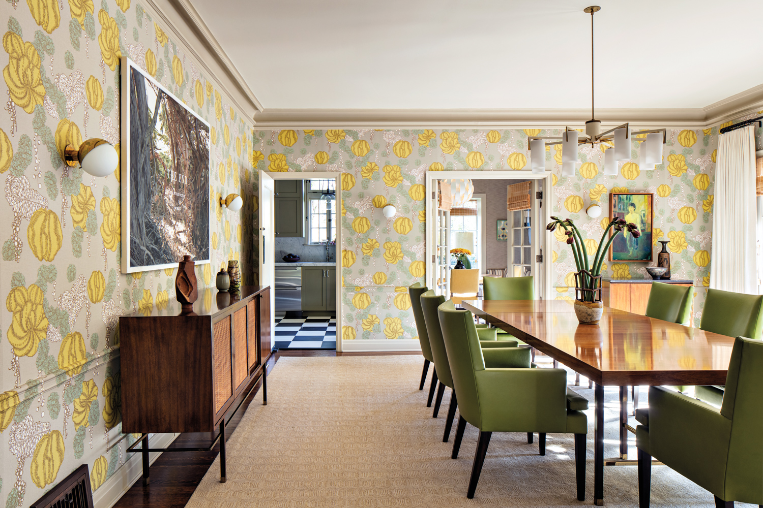 Dining room with long walnut table, green chairs, vintage white modern chandelier and graphic wallpaper with yellow touches.