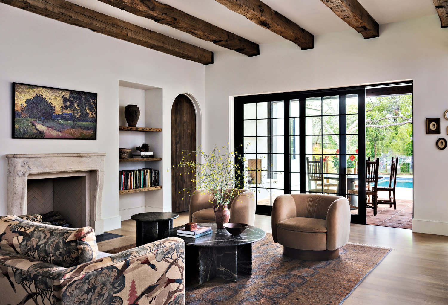A living room with two swivel chairs, a set of nesting tables, a sofa and built-in shelves with books.