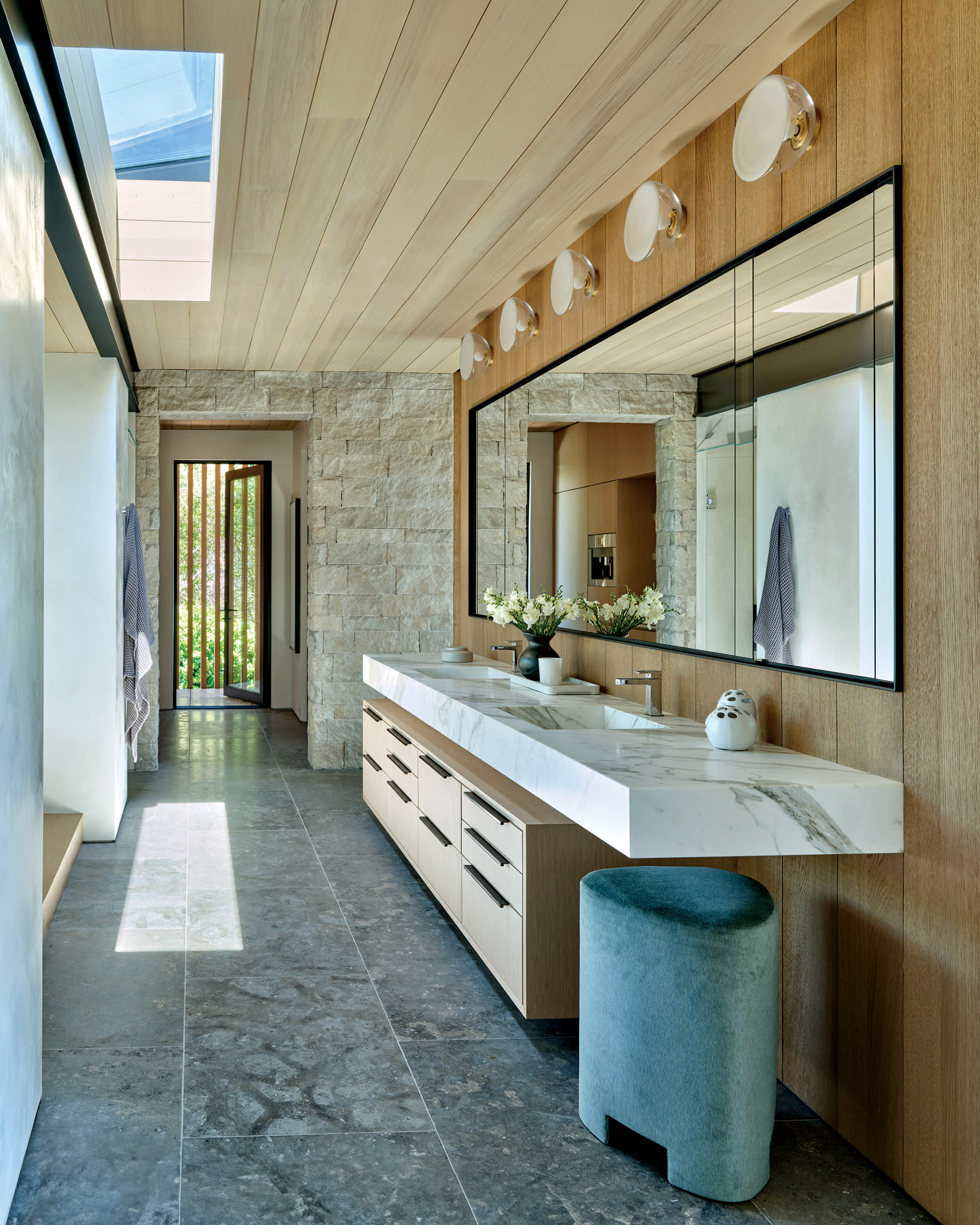 neutral organic bathroom marble-topped vanity on dark stone tile and against light wood paneling