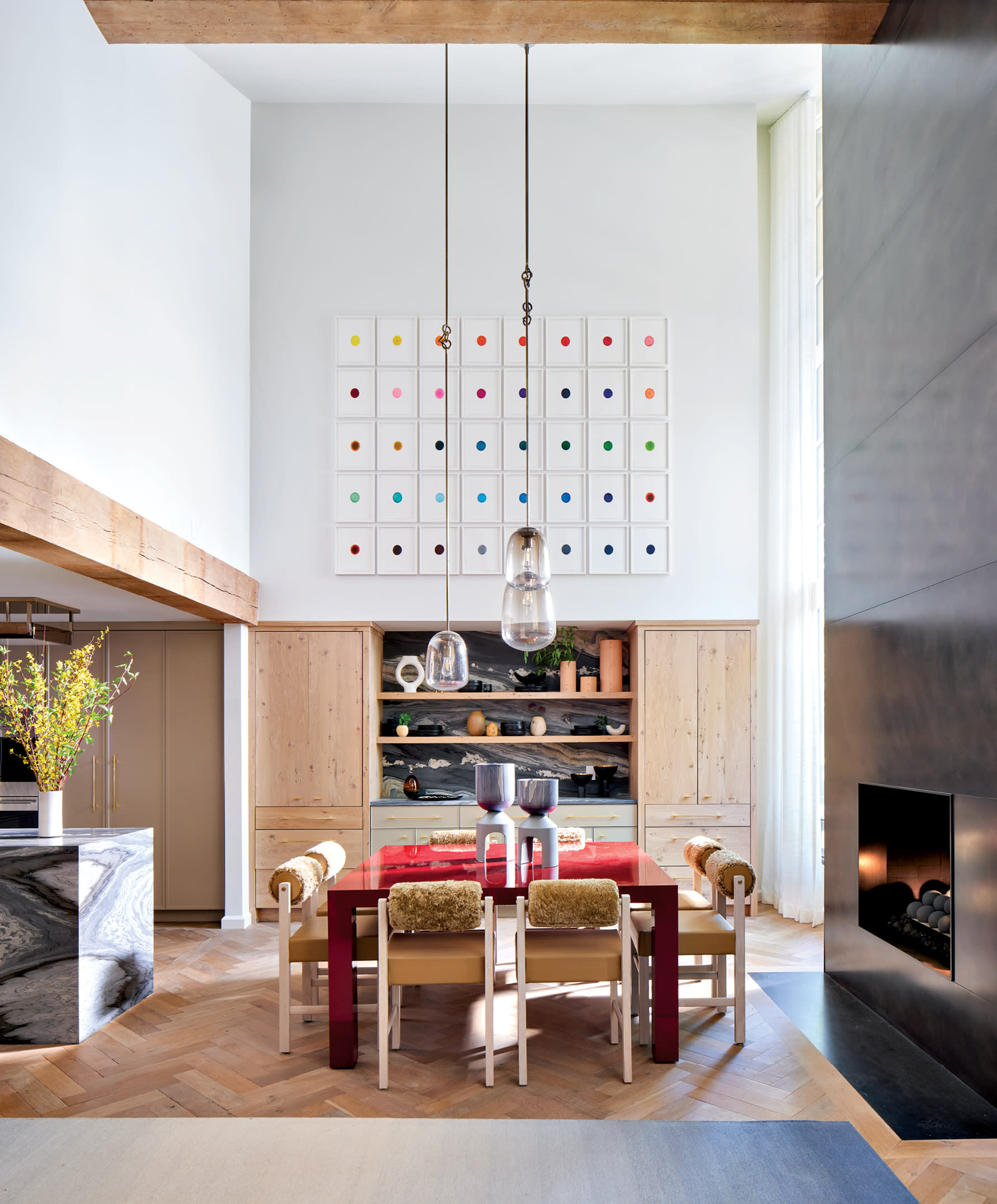 art-filled dining room with a red table and a dark steel fireplace