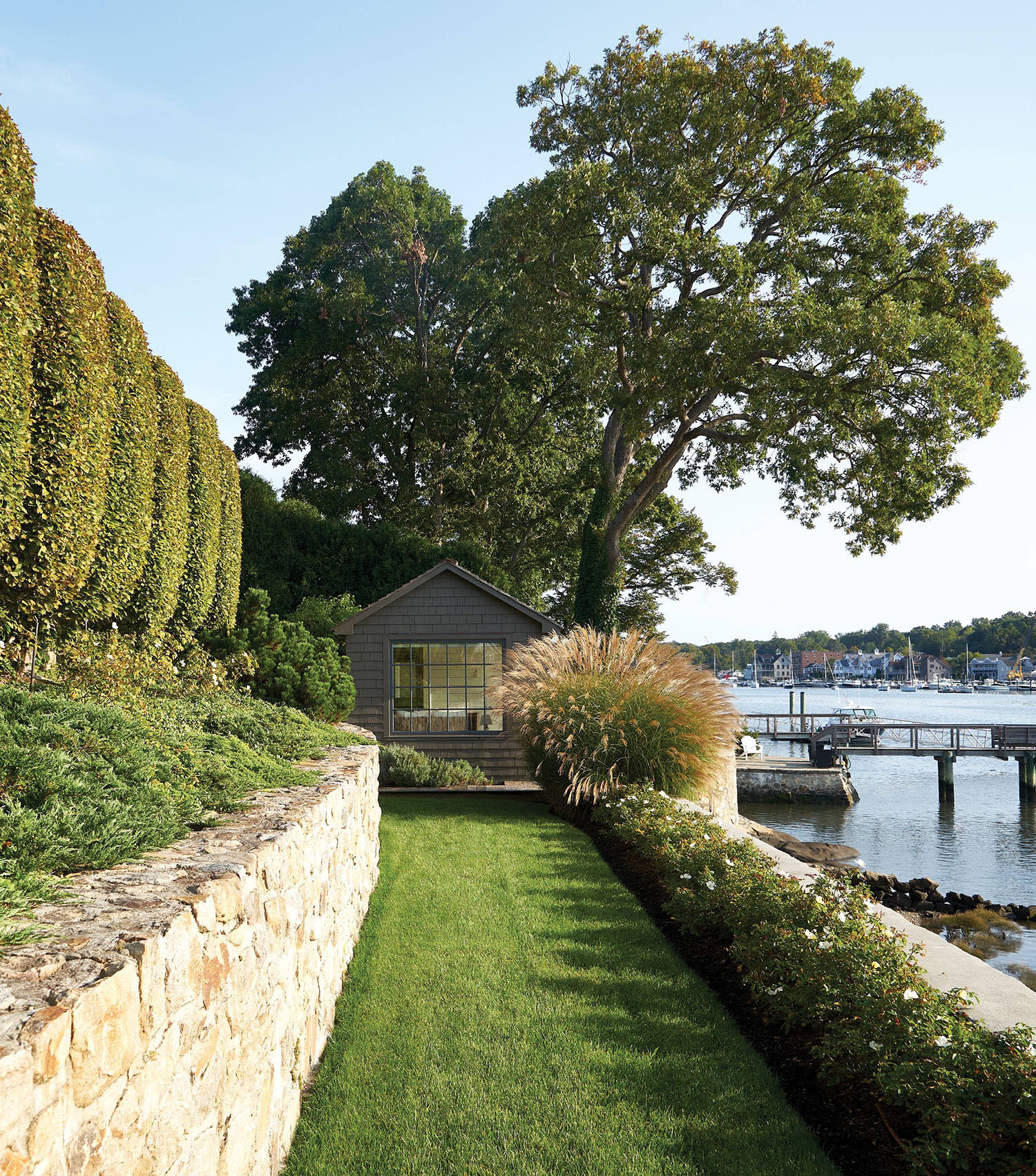 manicured path rimmed by boxwoods and beach grasses leading to a charming boathouse