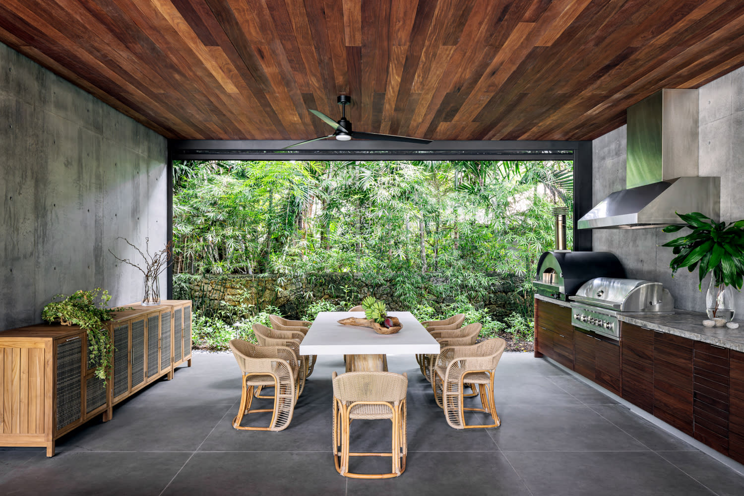 An outdoor kitchen and dining space featuring a table and chairs beneath a warm wood ceiling, creating a cozy atmosphere.