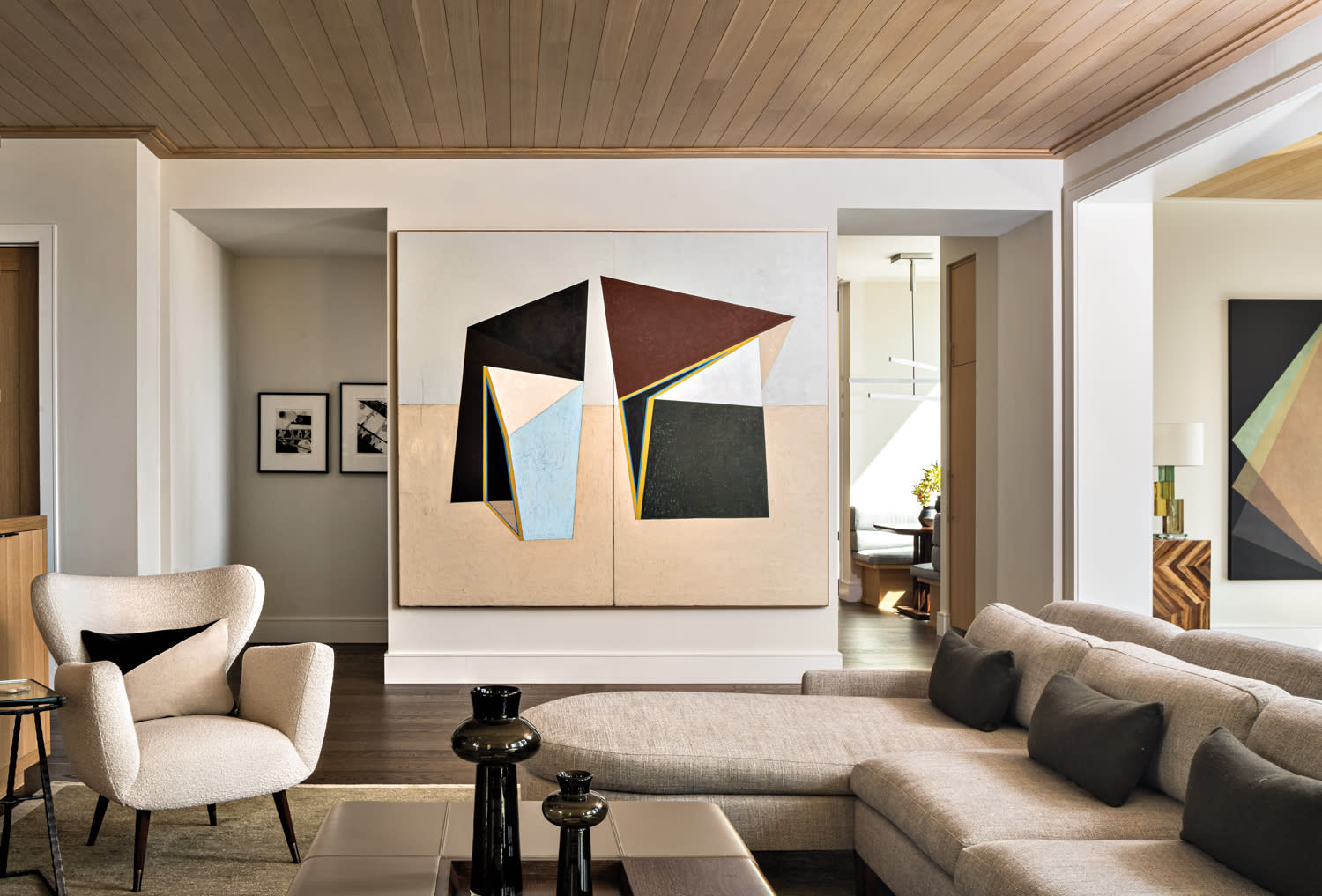 living room with bold modern artwork, tan sofa and black vases atop an ottoman